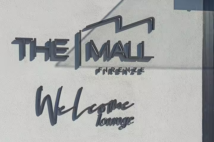 Entrance sign for The Mall Firenze welcome lounge, starting point for a luxury outlet shopping tour with Prada and Gucci