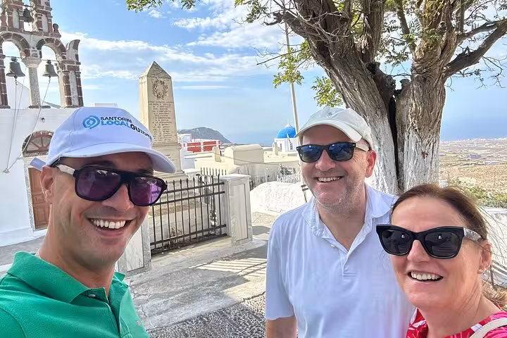 Happy travelers with local guide by Santorini chapel viewpoint during Thera one-day tour with lunch and wine tasting