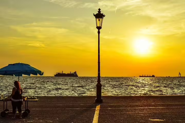Sunset over Thessaloniki waterfront with a silhouette of a street vendor and ships, ideal for a private custom night tour.