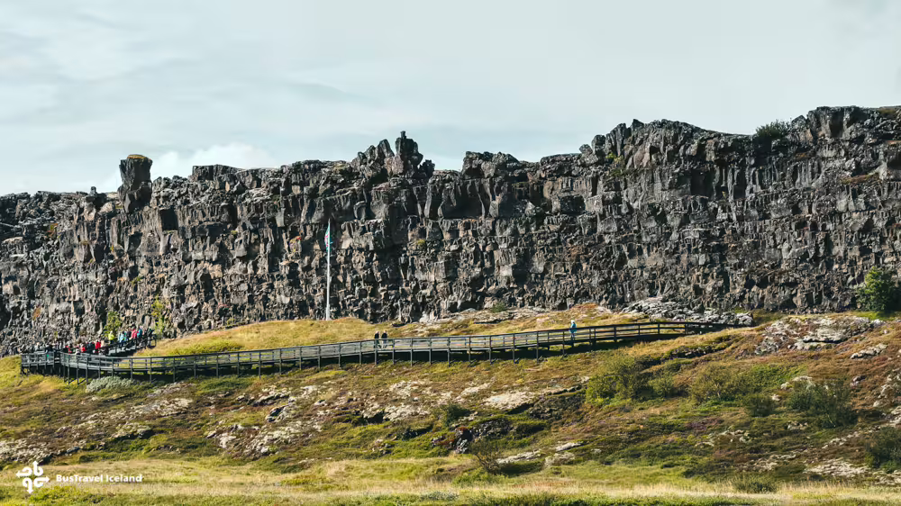 Wooden boardwalk along Almannagjá fault wall at Þingvellir National Park, Iceland, with visitors exploring the rocky cliffs