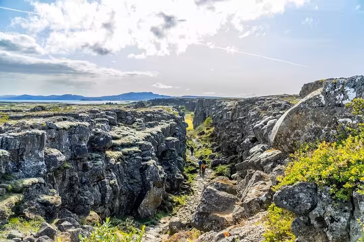 Hikers walking through rocky canyon fissure at Þingvellir National Park on Golden Circle tour, Iceland
