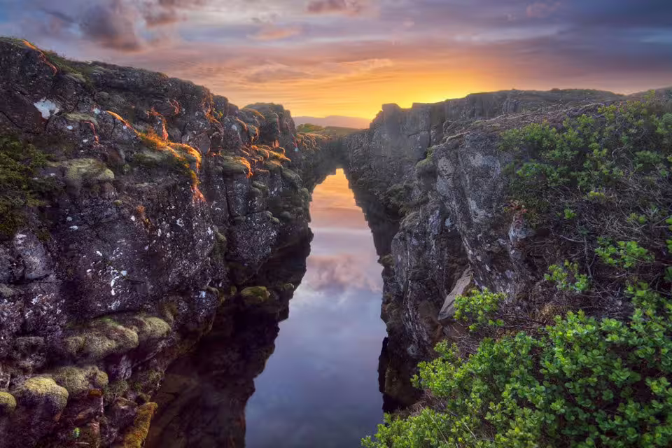 Dramatic rocky canyon with reflective water and golden sunset sky at Þingvellir on Iceland's Golden Circle