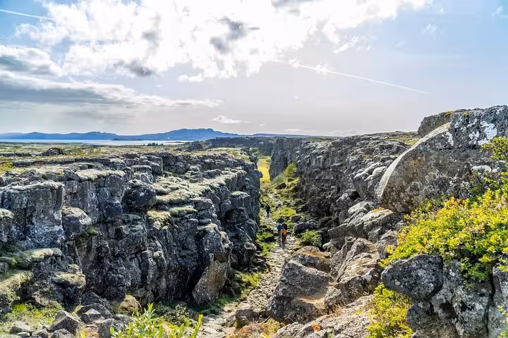 Hikers walking through rocky Þingvellir canyon rift valley with Icelandic landscape in background