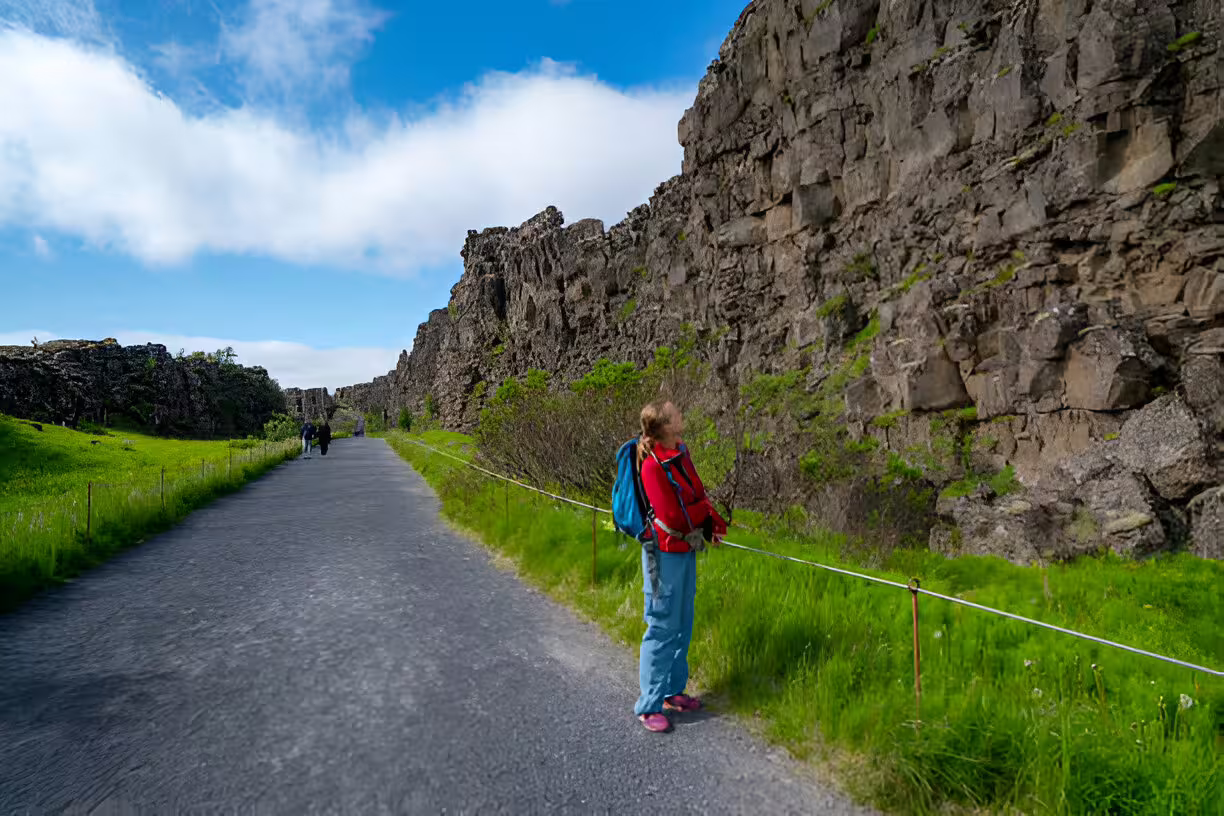 Hiker in red jacket walking along Þingvellir canyon path on Golden Circle tour from Reykjavik