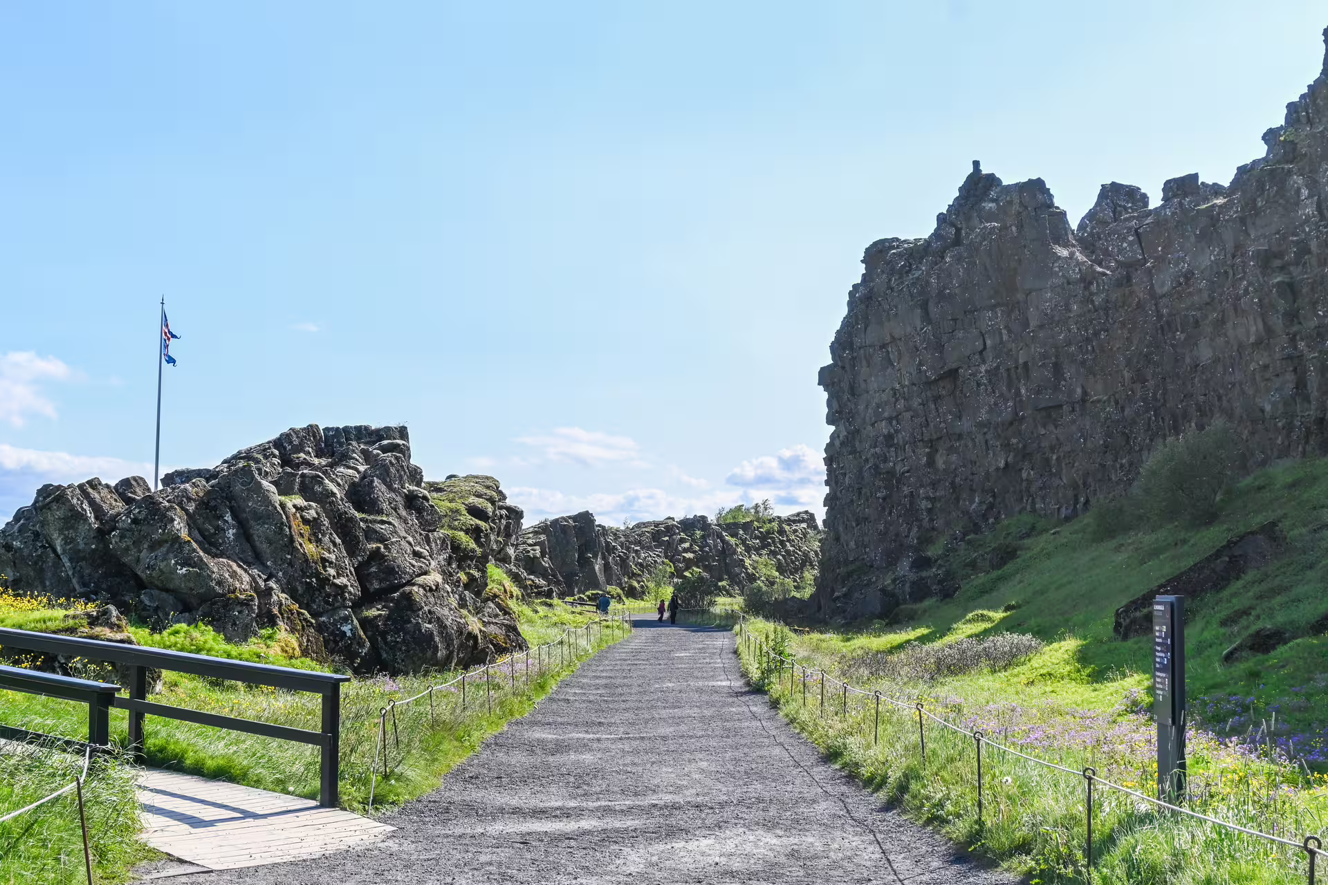 Gravel path through Þingvellir lava rock canyon with Icelandic flag, Ring Road Iceland tour