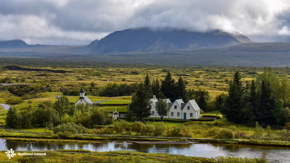 Thingvellir National Park church and farmhouse beside river with dramatic mountain backdrop, Iceland
