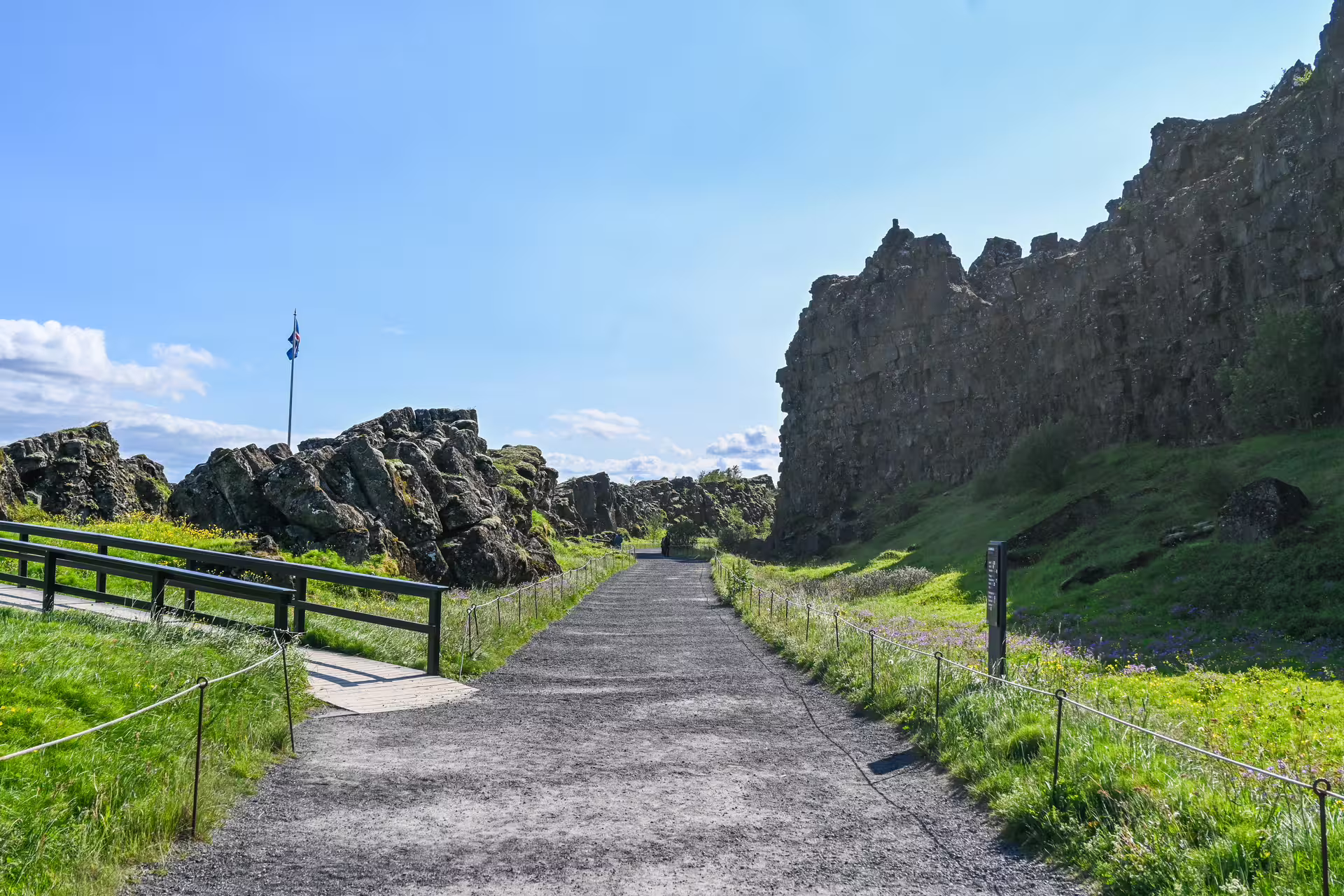 Gravel walking path through Þingvellir lava rock formations with Icelandic flag on Iceland Ring Road tour
