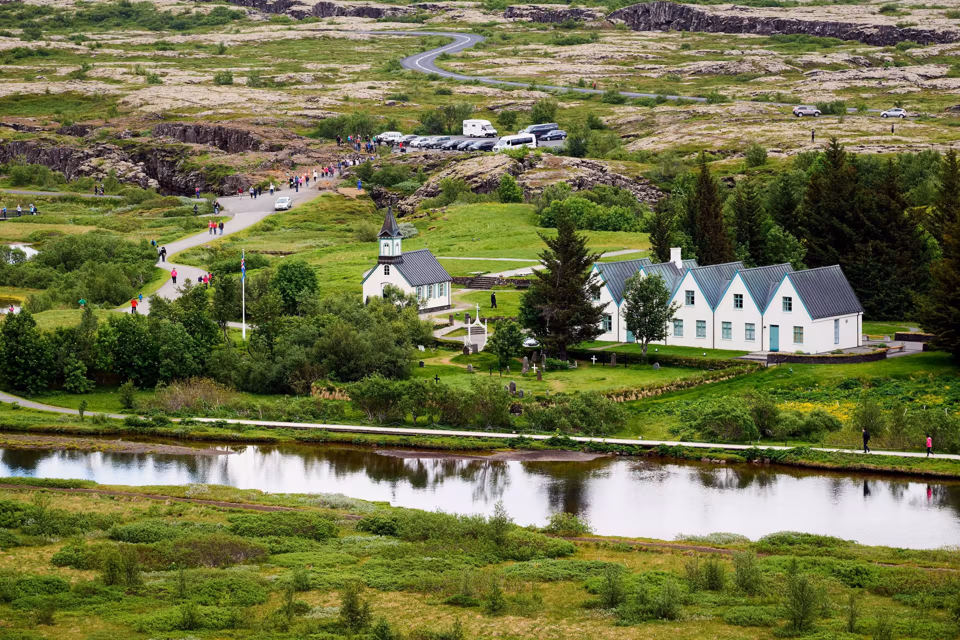 Panoramic view of Þingvellir National Park with historic church, lush greenery, and winding paths.