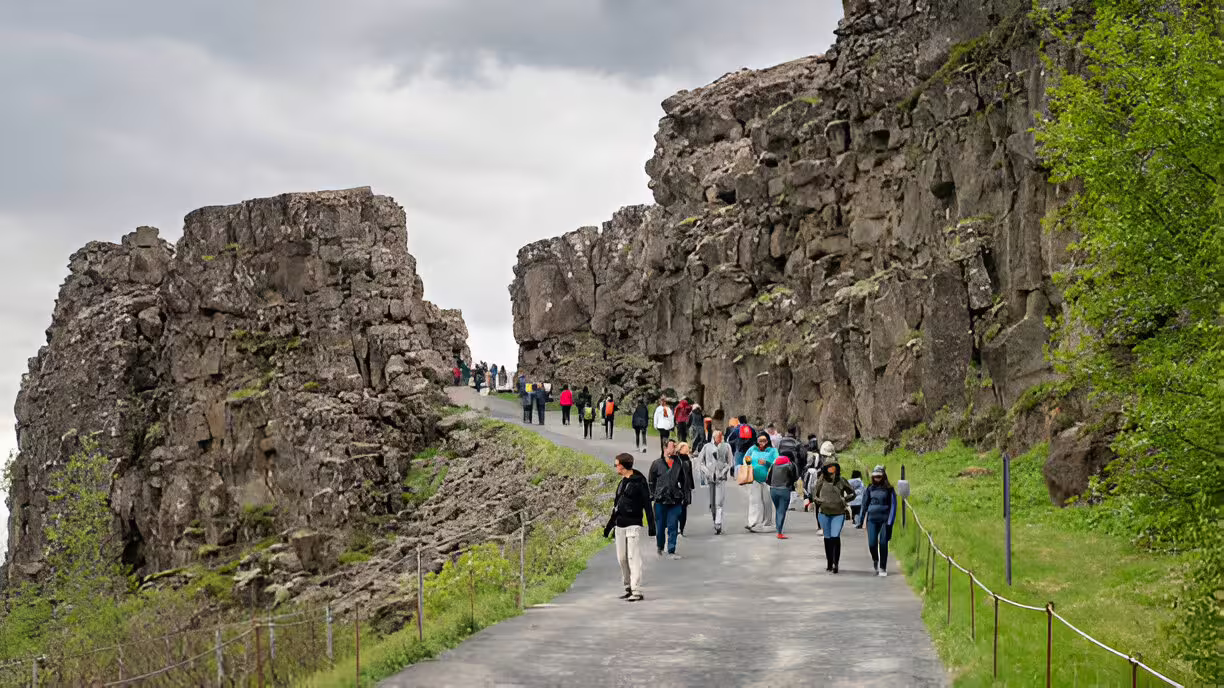 Tourists walking along a paved path through the dramatic lava rock cliffs at Þingvellir National Park, Iceland