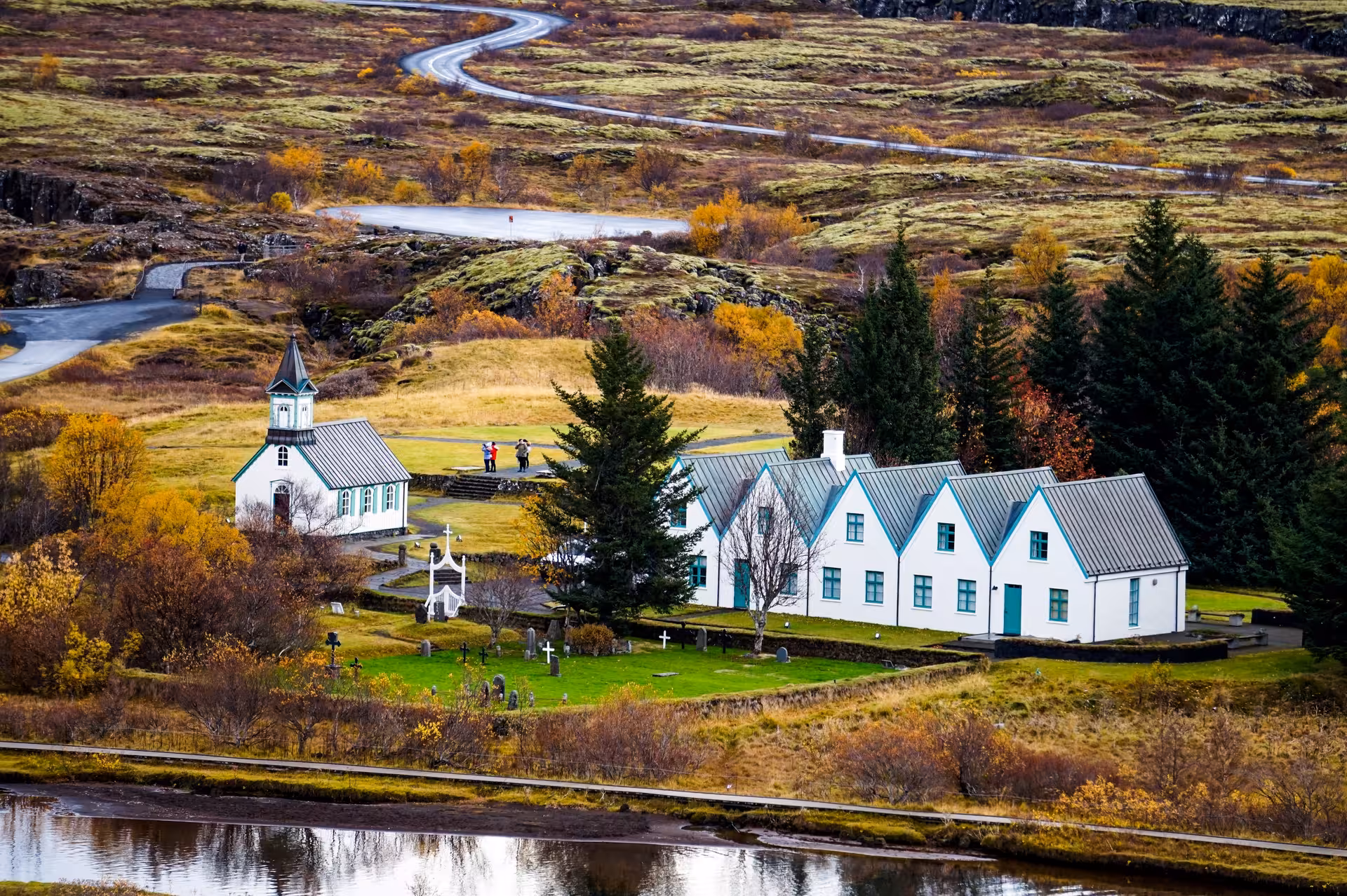 Scenic view of a historic church and houses in Thingvellir National Park, Iceland, surrounded by autumn foliage.
