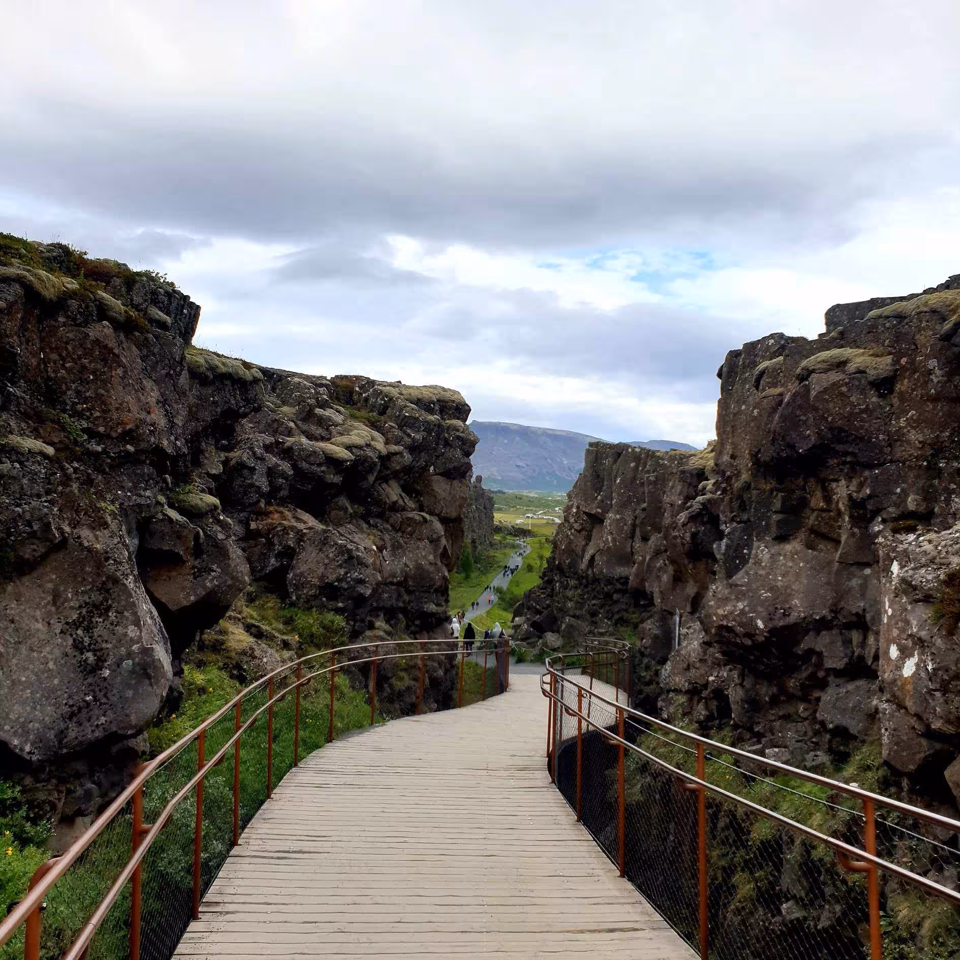 Wooden boardwalk through Þingvellir tectonic rift canyon with green valleys and mountains, Iceland