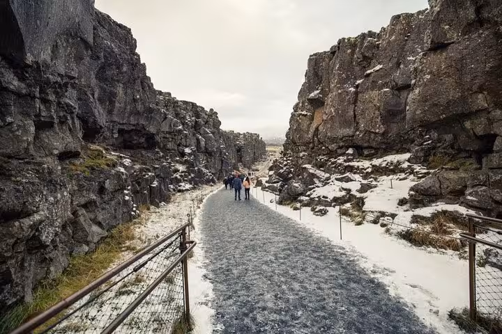 Hikers walking through Þingvellir rift valley canyon between towering snow-dusted rock walls, Iceland