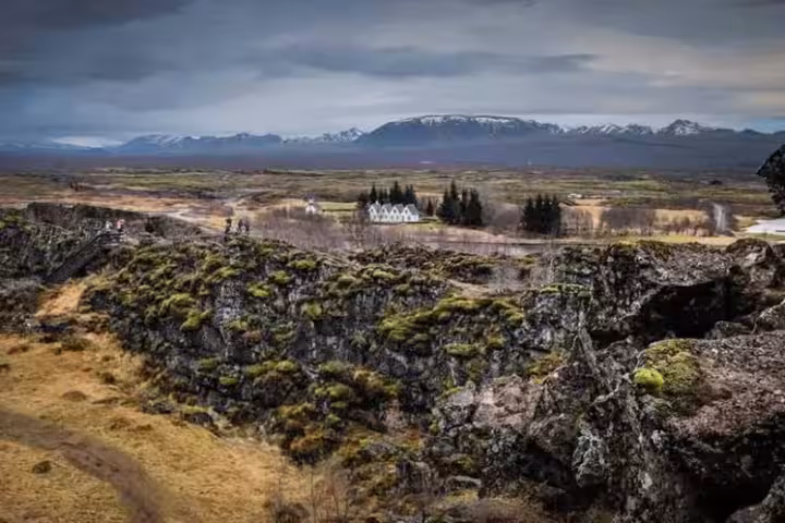 Þingvellir rift valley with moss-covered lava rocks, white farmhouse, and snow-capped mountains in Iceland