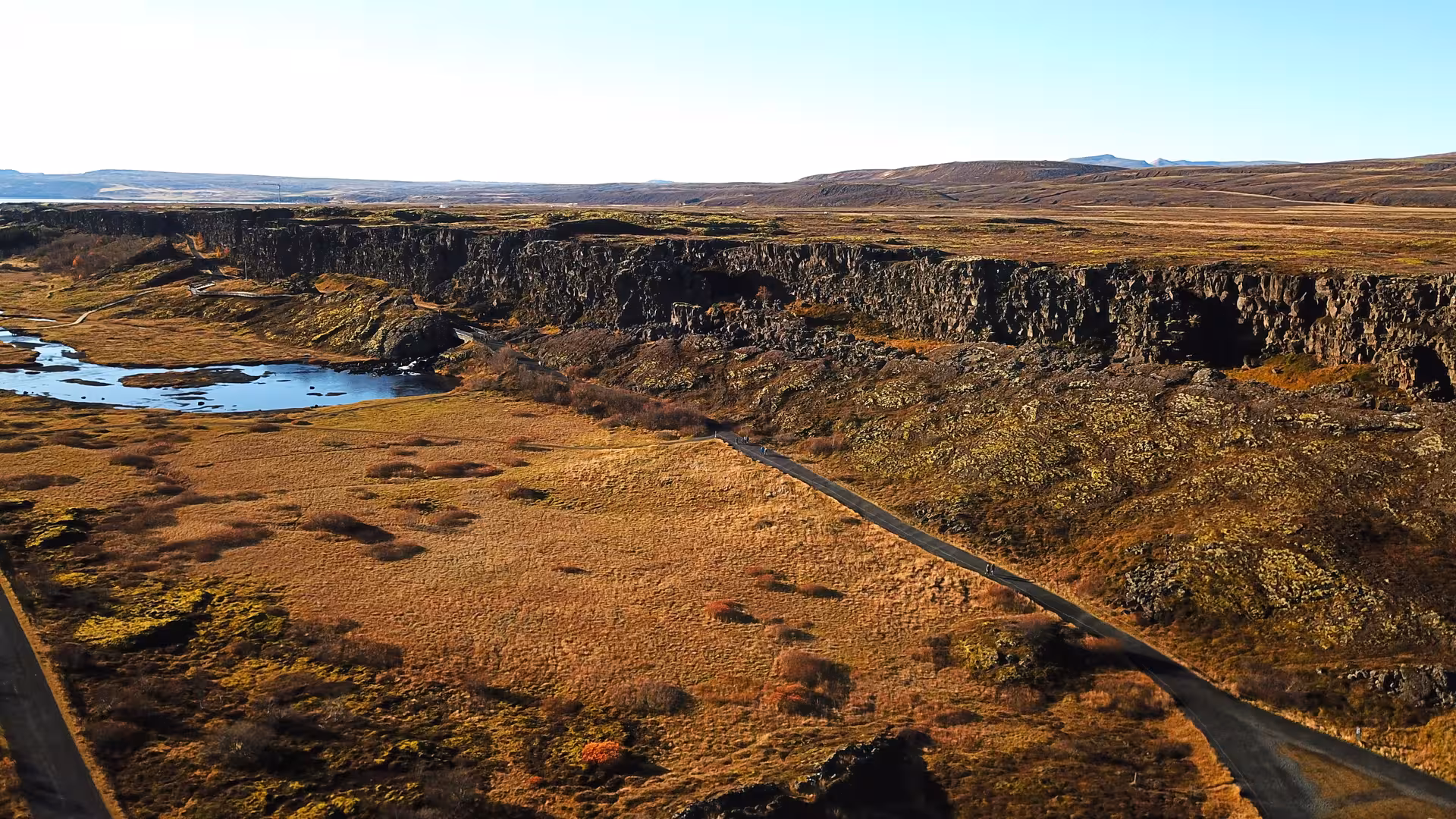 Aerial view of Þingvellir rift valley with rocky cliffs, golden tundra, and winding path in Iceland