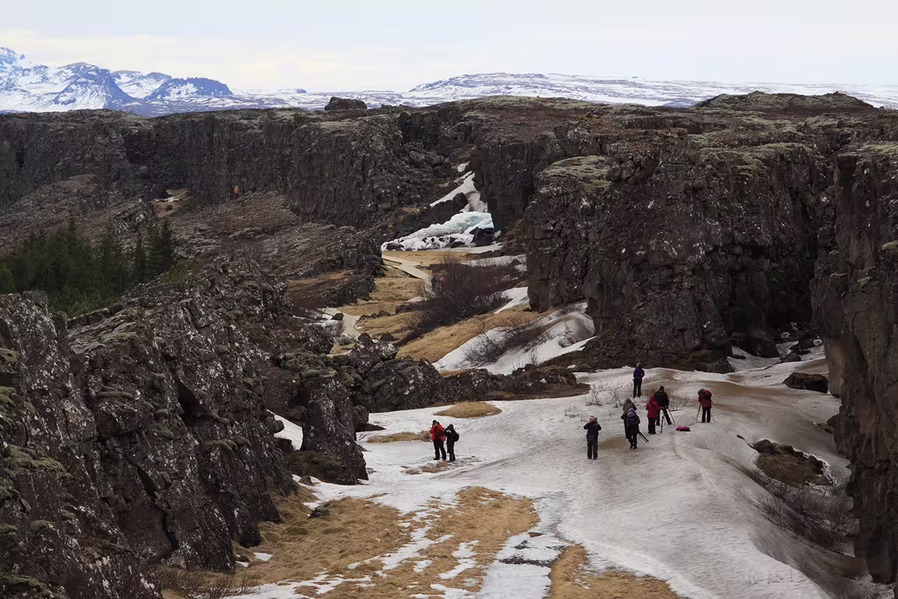 Tourists exploring Þingvellir canyon rift valley with snow and rocky cliffs on Iceland's Golden Circle