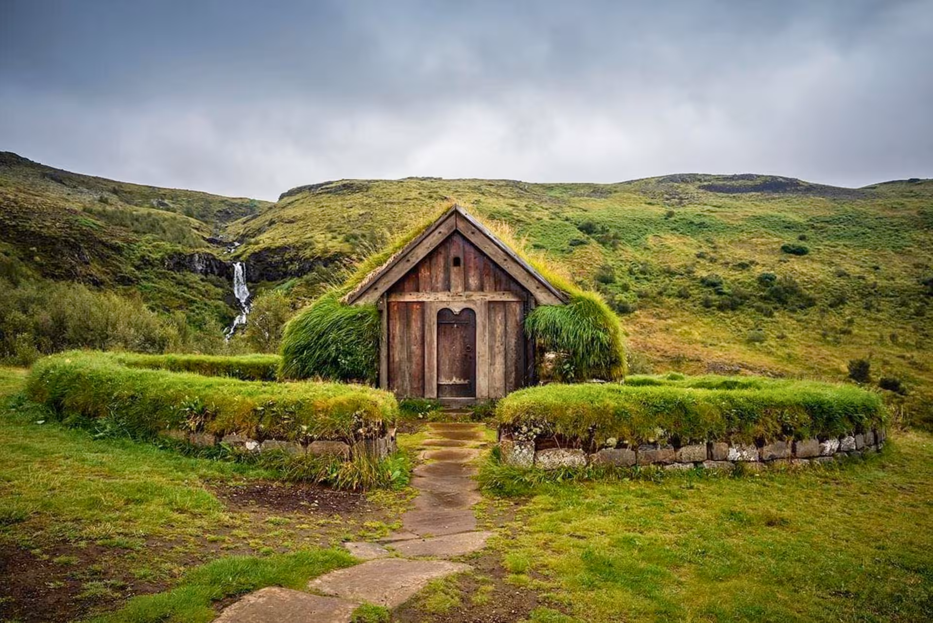 Þjórsárdalur Valley private tour stop at Stöng turf house with green hills and a small waterfall behind