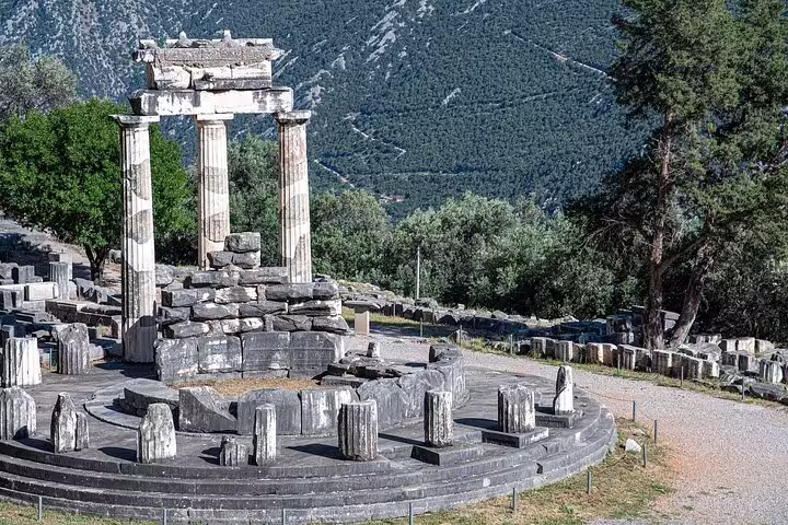 Ancient ruins of the Tholos of Delphi surrounded by lush greenery and mountains, perfect for a historical tour from Athens.