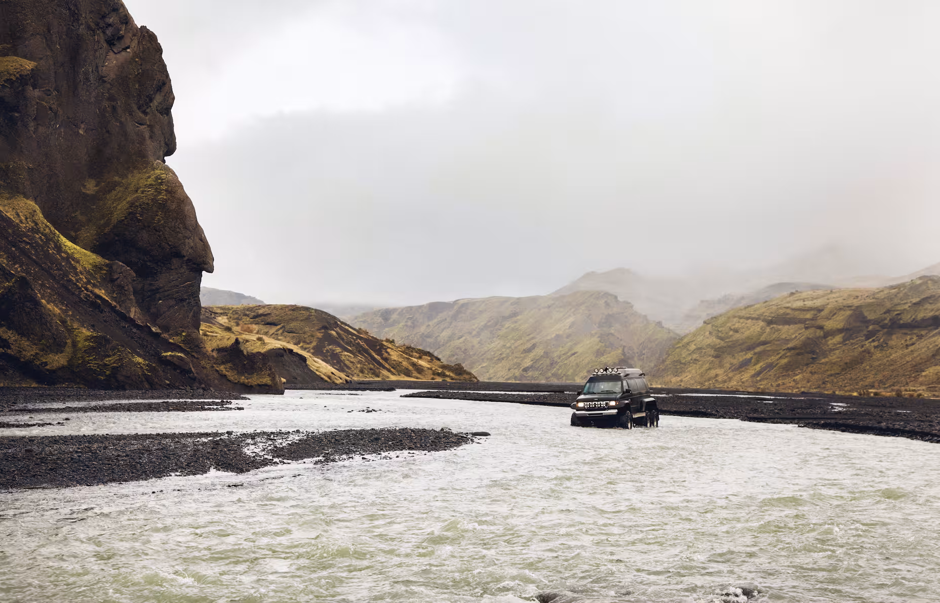 Black 4x4 SUV fording a glacial river in Thorsmork valley surrounded by green mountains