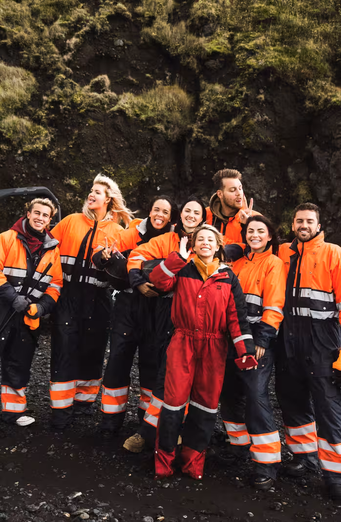 Group of eight people in orange and red safety suits posing at Iceland black sand beach near rocky cliffs