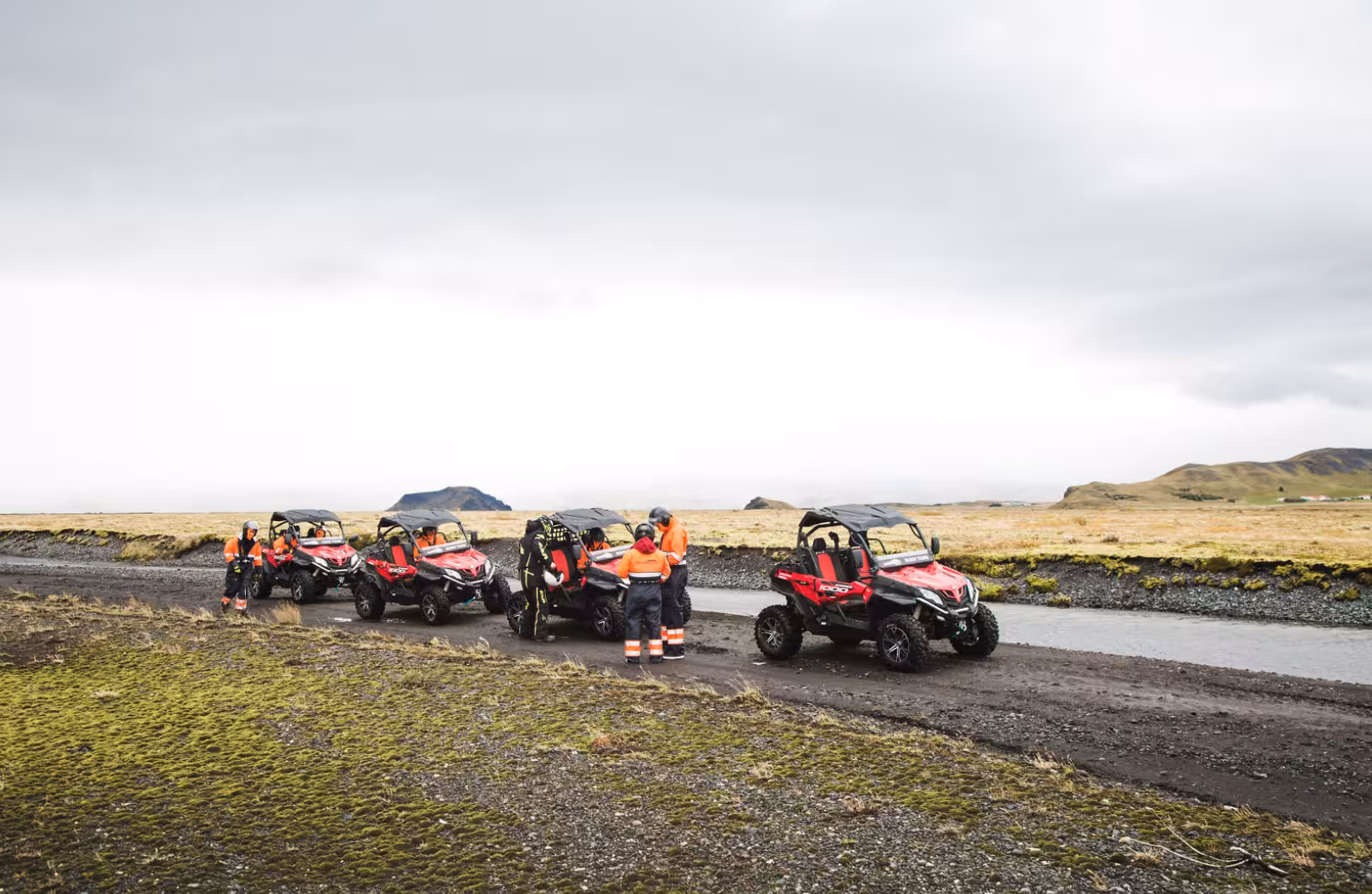 Group of riders with red buggy UTVs parked on a dirt track in Iceland's highland landscape