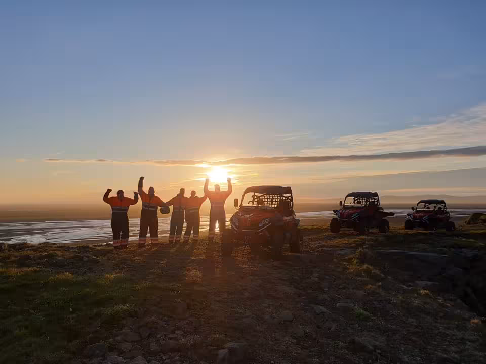 Group of five people celebrating at sunset beside red buggy vehicles on Iceland highland terrain