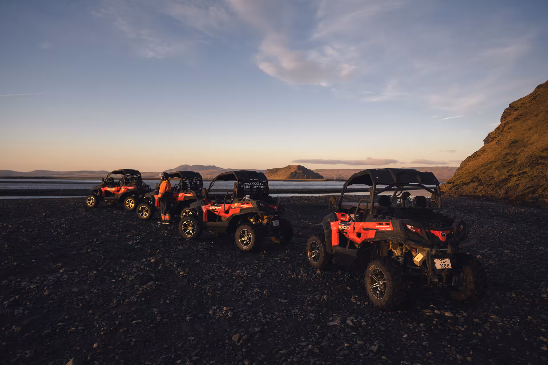 Three red CFMOTO buggy UTVs parked on Iceland's black sand beach at sunset with mountains in background