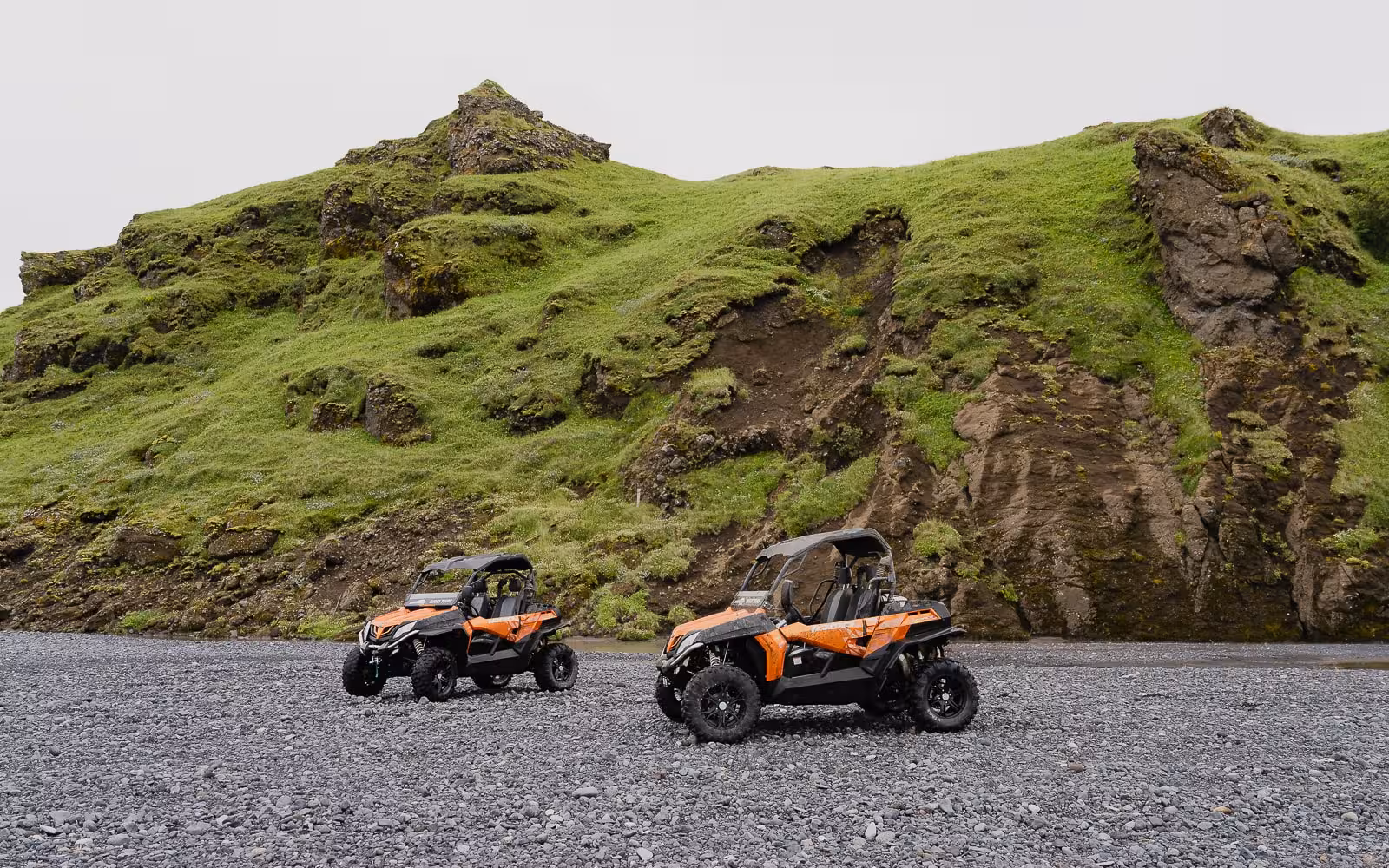 Two orange buggies parked on rocky terrain below green moss-covered cliffs in Thorsmork Iceland highlands
