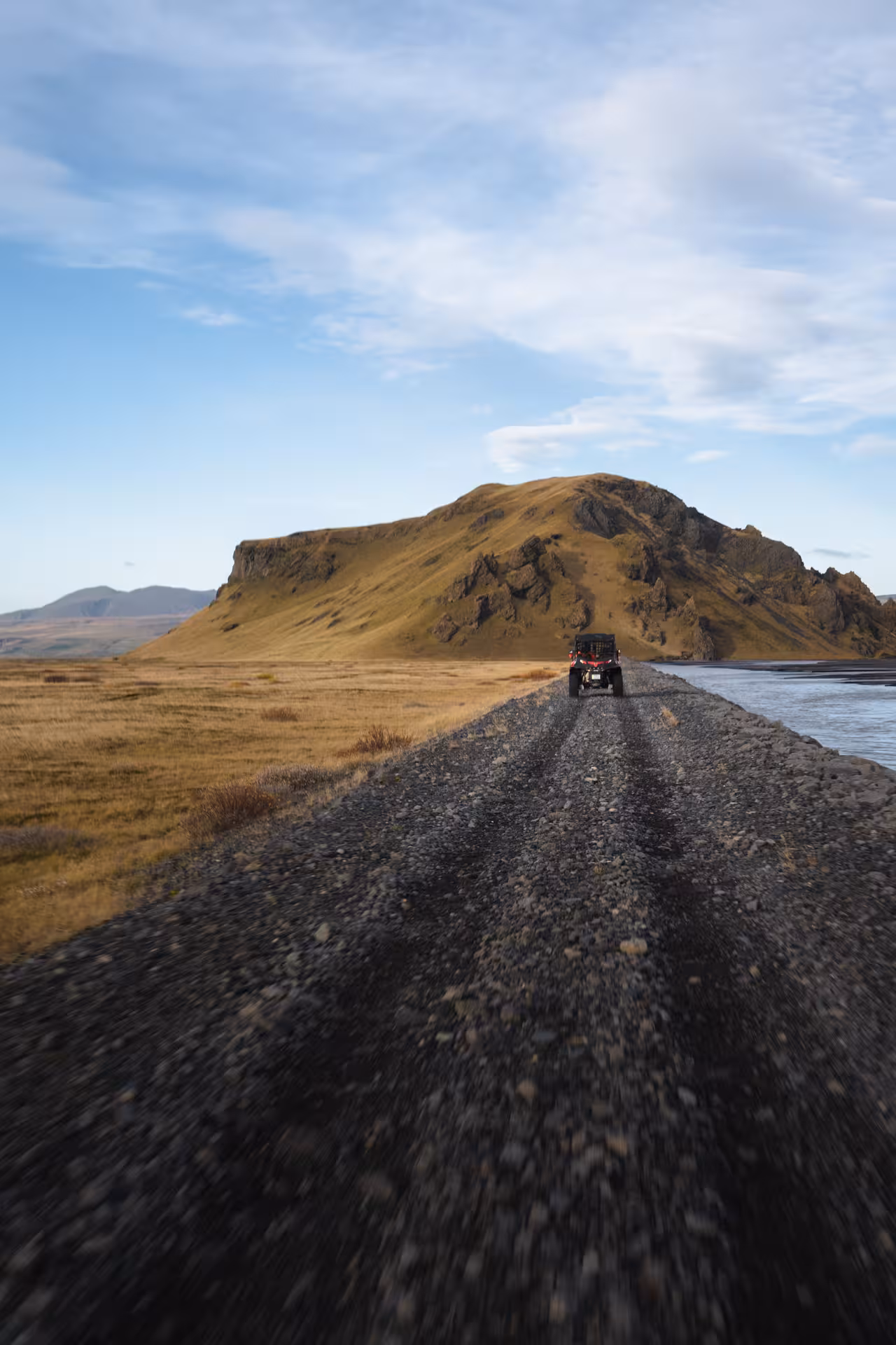 Red buggy driving on gravel trail toward volcanic mountain in Thorsmork Iceland highlands