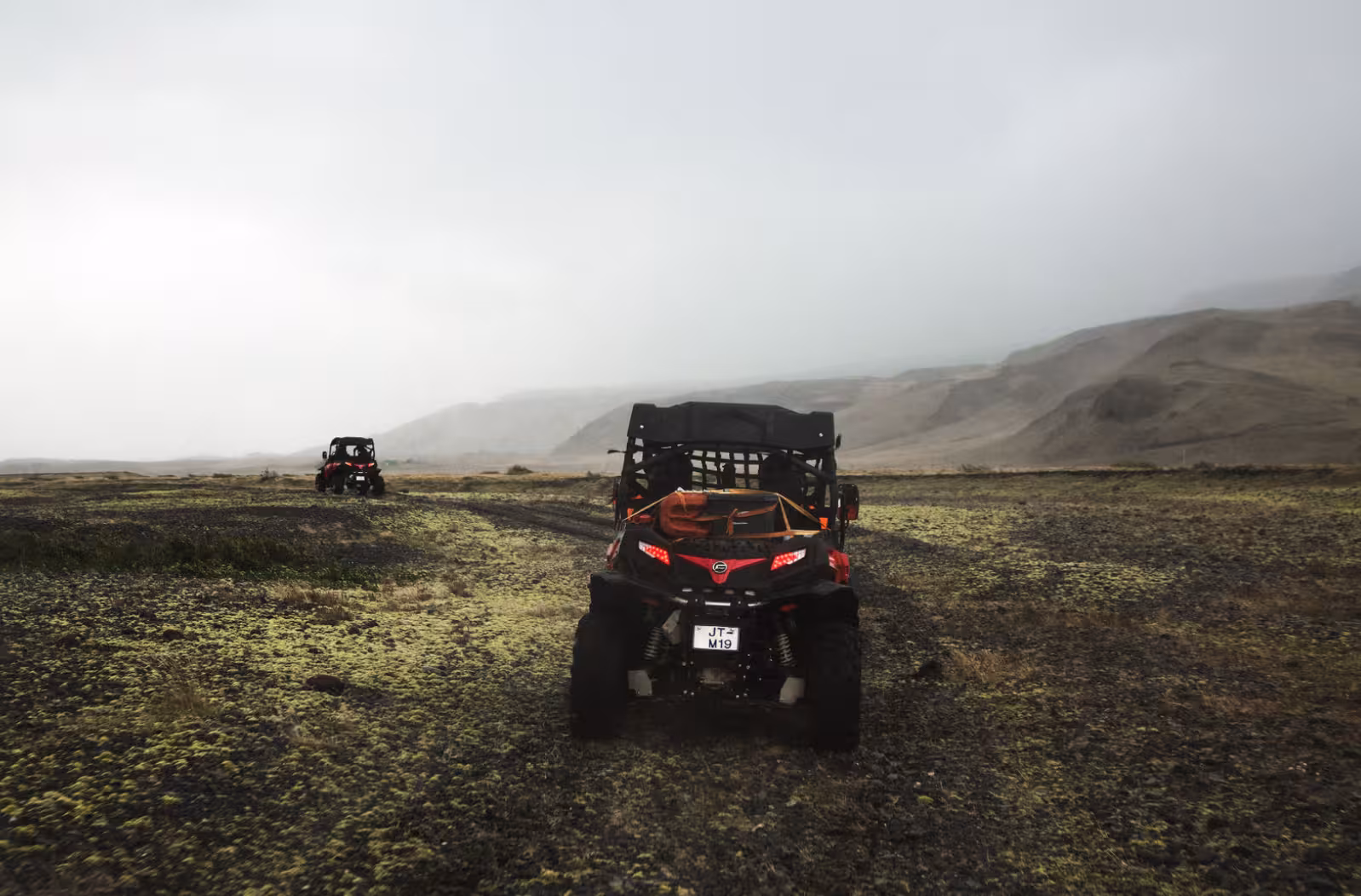 Two red Can-Am buggies driving through mossy lava fields in Iceland's misty highlands near Thorsmork