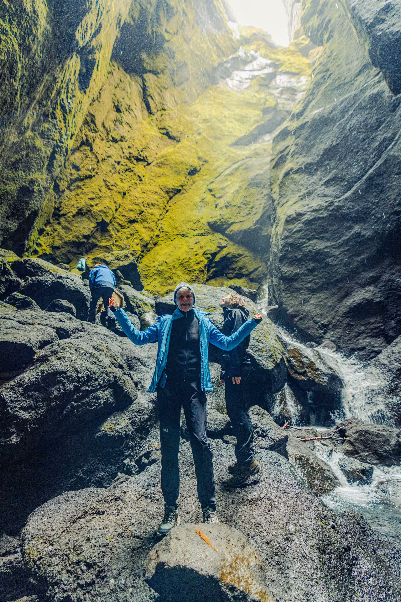 Hiker celebrating with arms raised inside Thorsmork canyon with mossy walls and stream