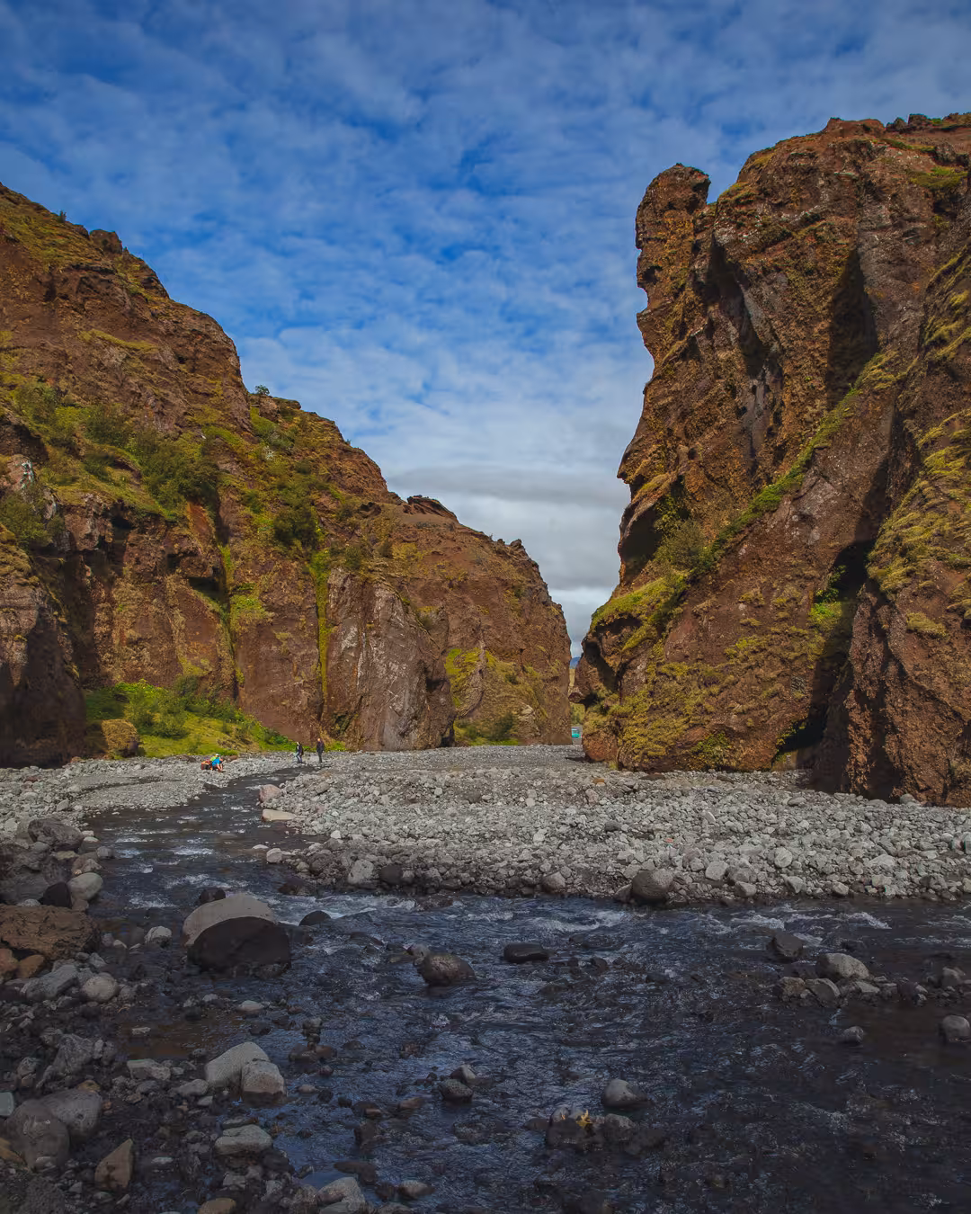 Rocky river canyon with towering moss-covered cliffs at Thorsmork, hikers visible in the distance