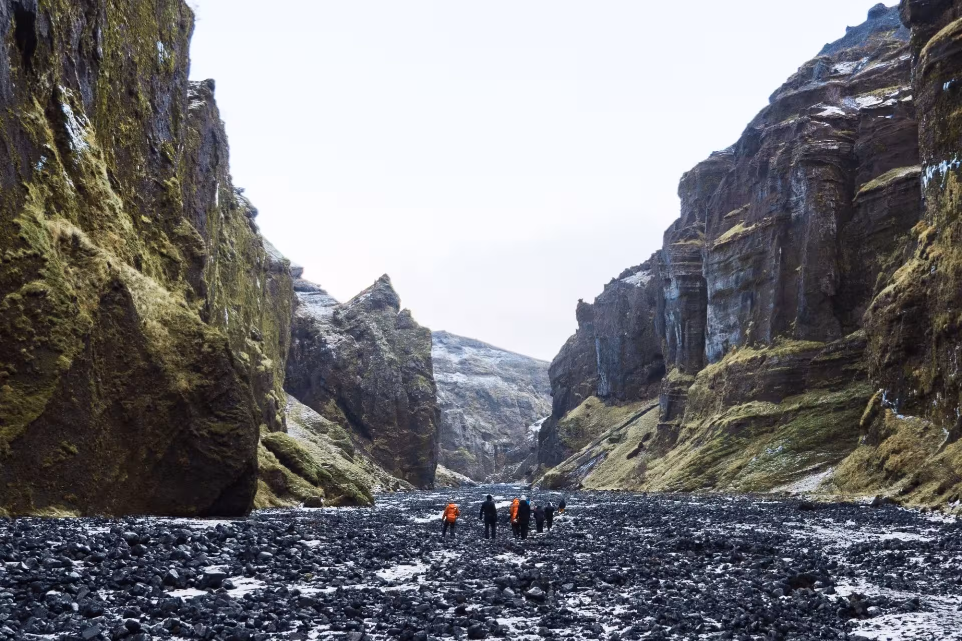 Hikers walking through Thorsmork canyon with towering moss-covered basalt cliffs and rocky riverbed in Iceland