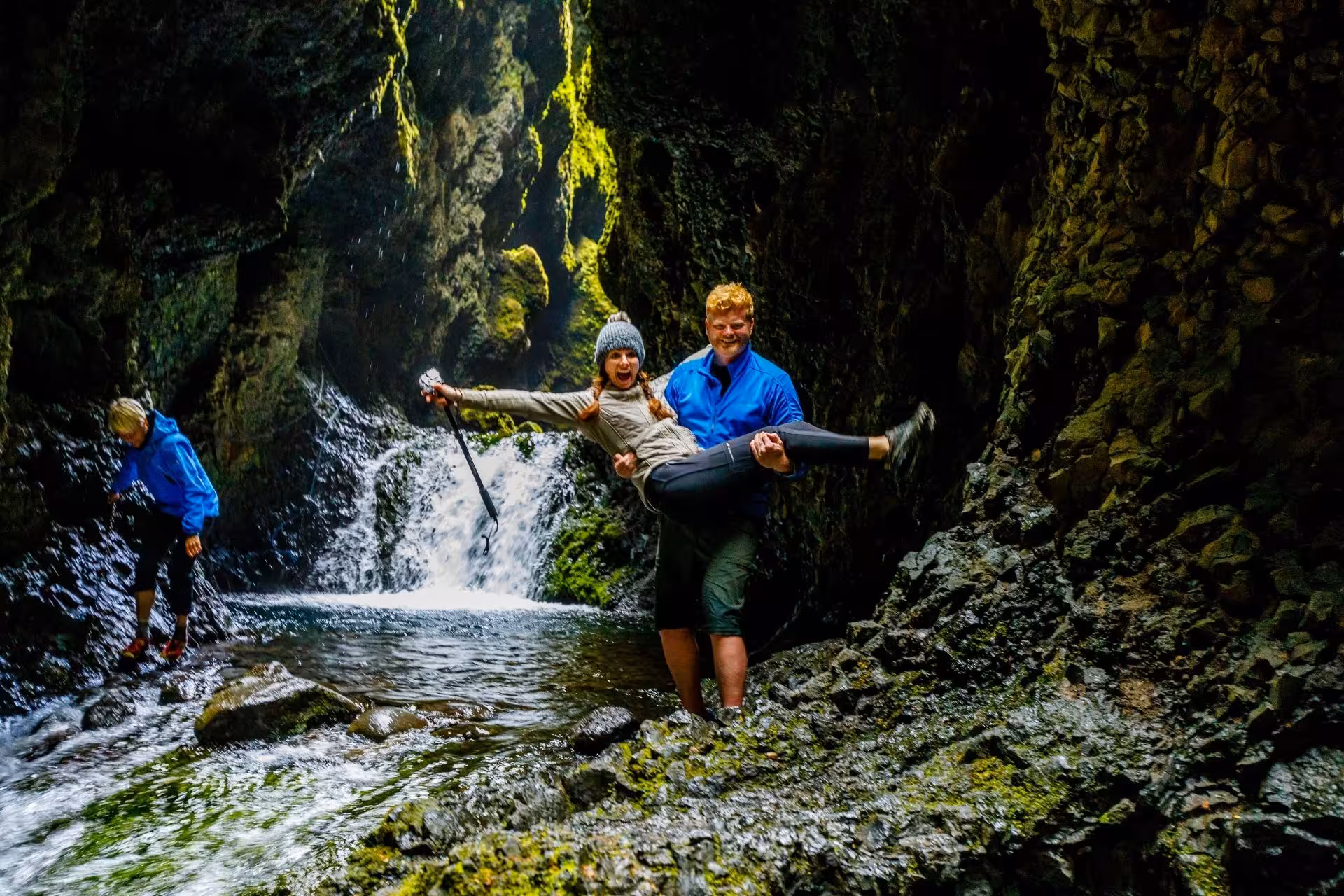 Couple laughing in Thorsmork canyon gorge with waterfall and mossy rocks
