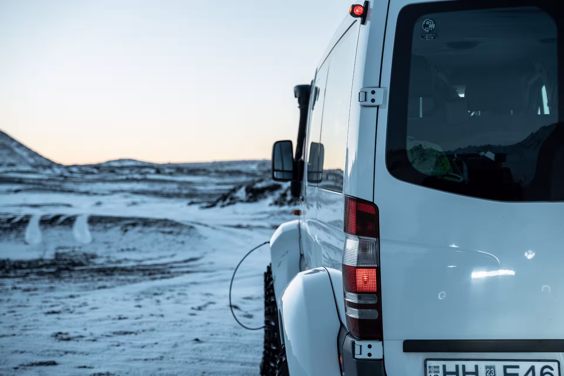 White 4WD van parked on snowy highland terrain in Iceland's volcanic wilderness at dusk