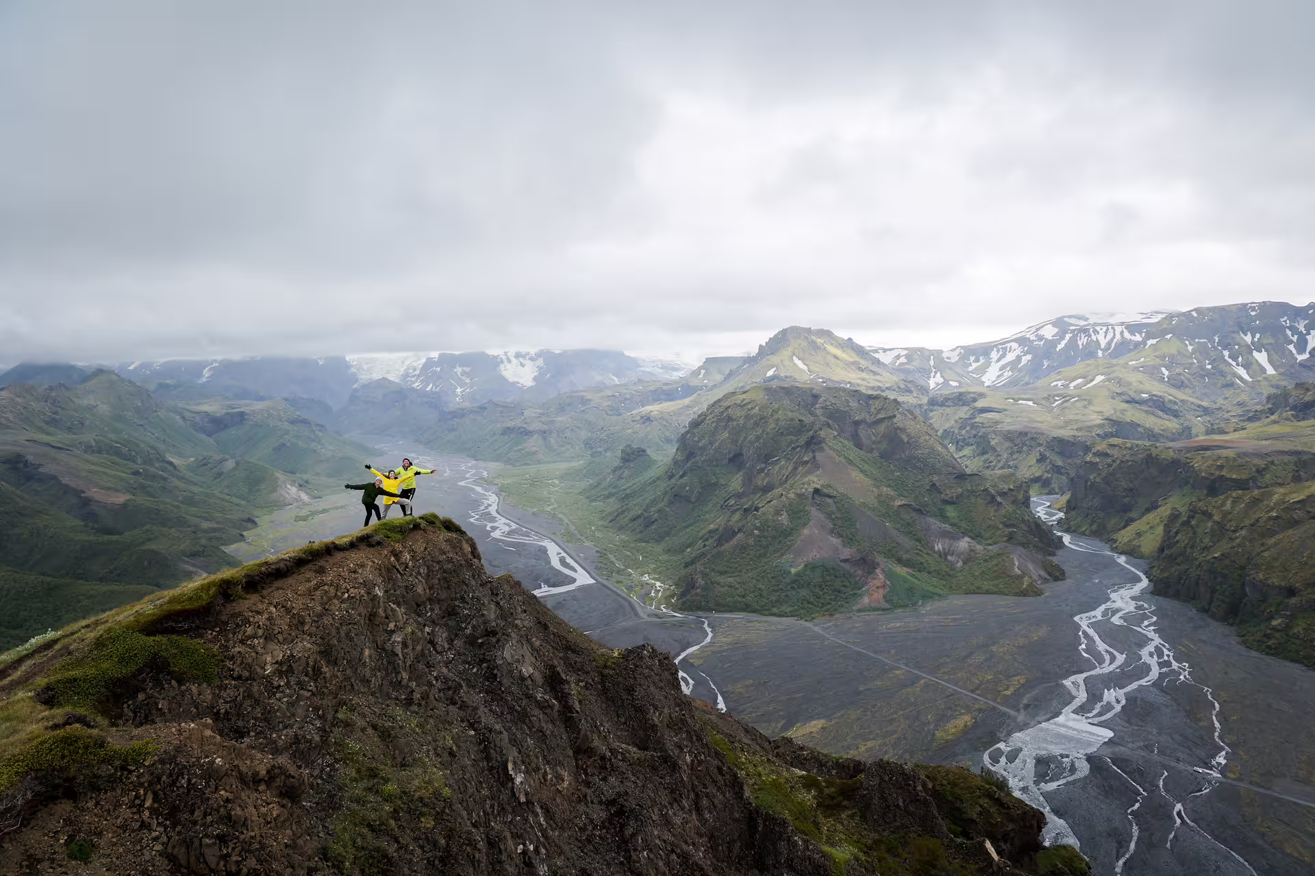 Two excited travelers stand atop a rocky cliff overlooking Thorsmork's stunning glacial valley on a full-day 4x4 Iceland tour.