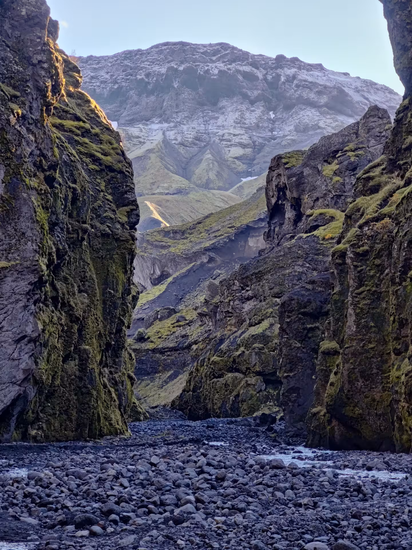Narrow black volcanic canyon with mossy walls leading to green valleys and snow-capped Thorsmork glacier in Iceland