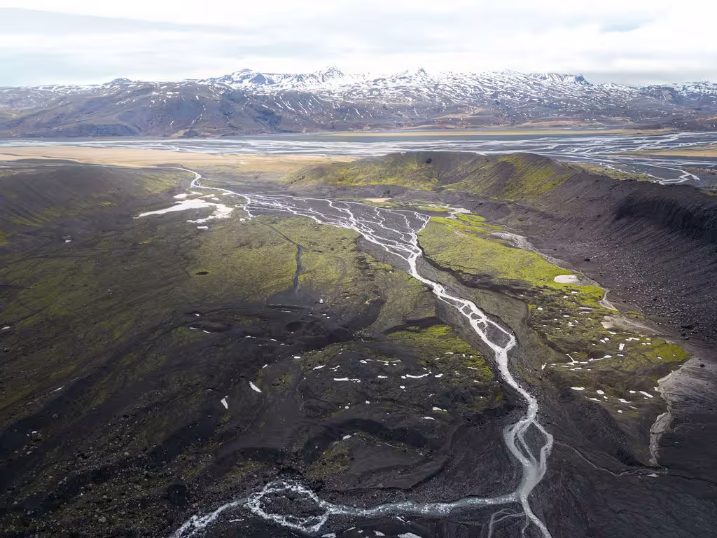 Aerial view of Thorsmork highland valley with braided glacial rivers, black volcanic terrain, and snow-capped mountains in Iceland
