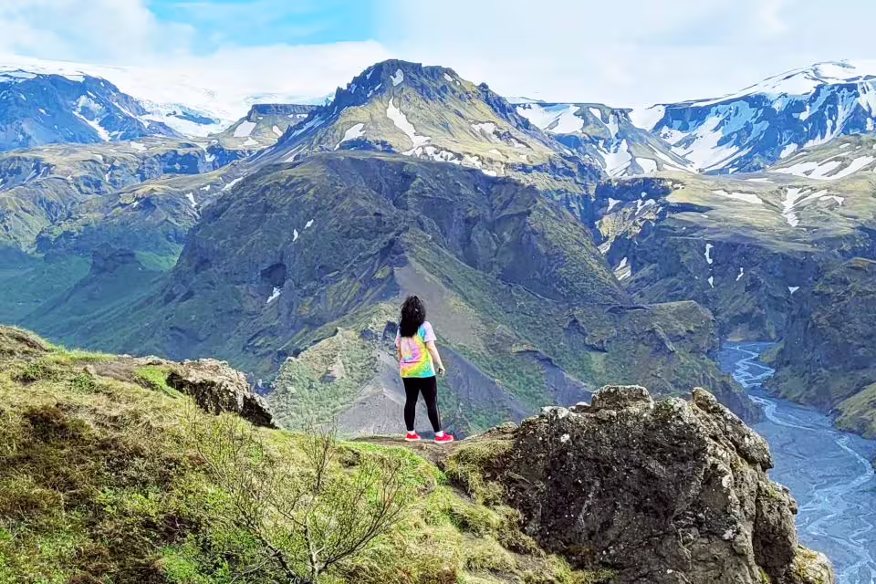 Hiker standing on rocky cliff overlooking Thorsmork valley with glaciers and snow-capped volcanic mountains