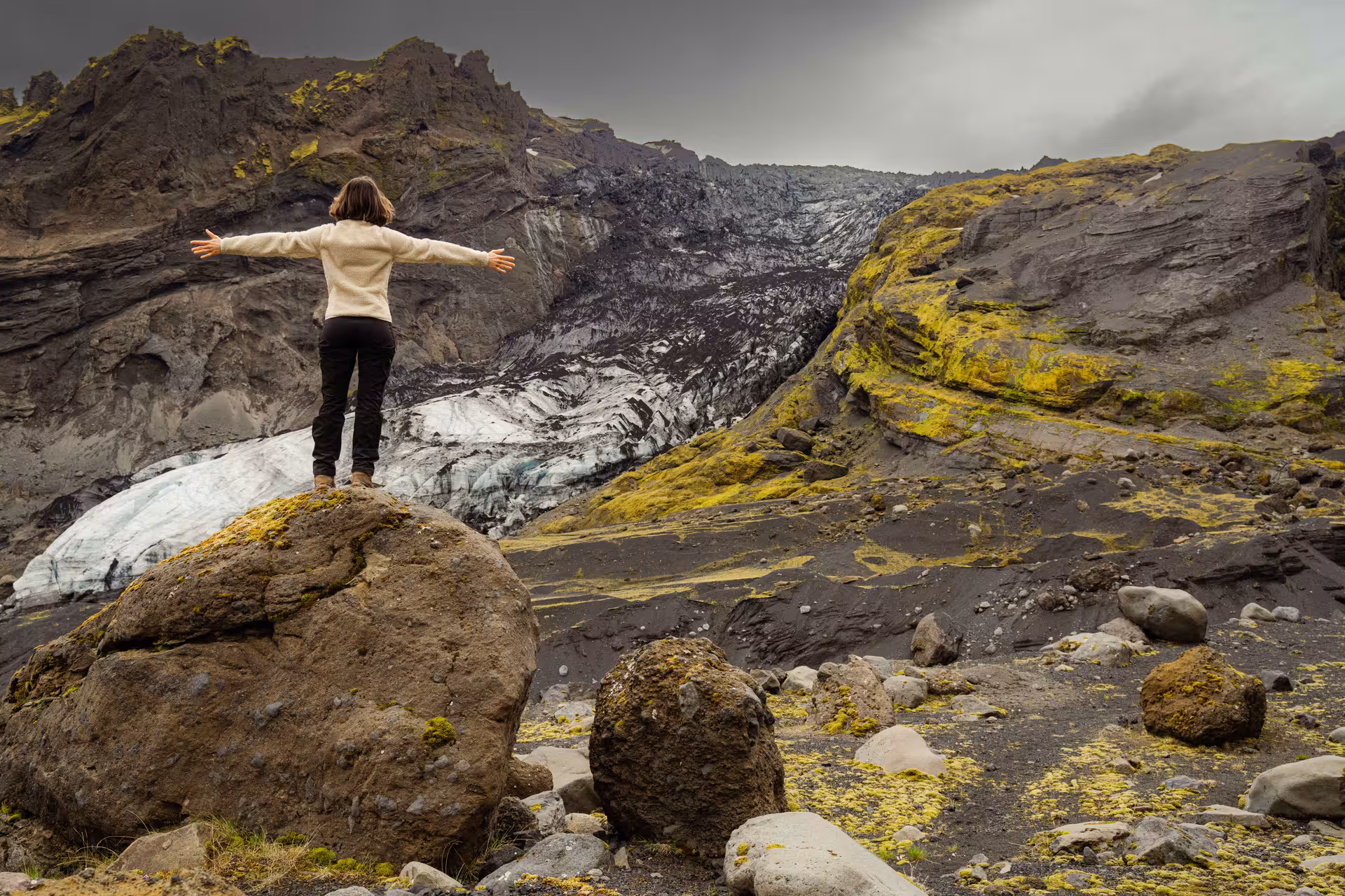 Hiker standing on rock with arms outstretched overlooking Thorsmork glacier and volcanic landscape Iceland