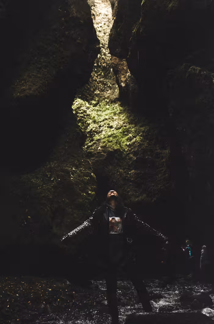 Hiker with arms outstretched gazing up in a moss-covered canyon gorge in Thorsmork Iceland
