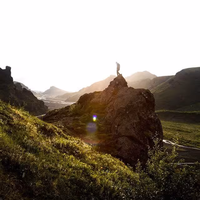 Hiker standing on rocky peak in Thorsmork valley surrounded by green hills and glaciers at sunset
