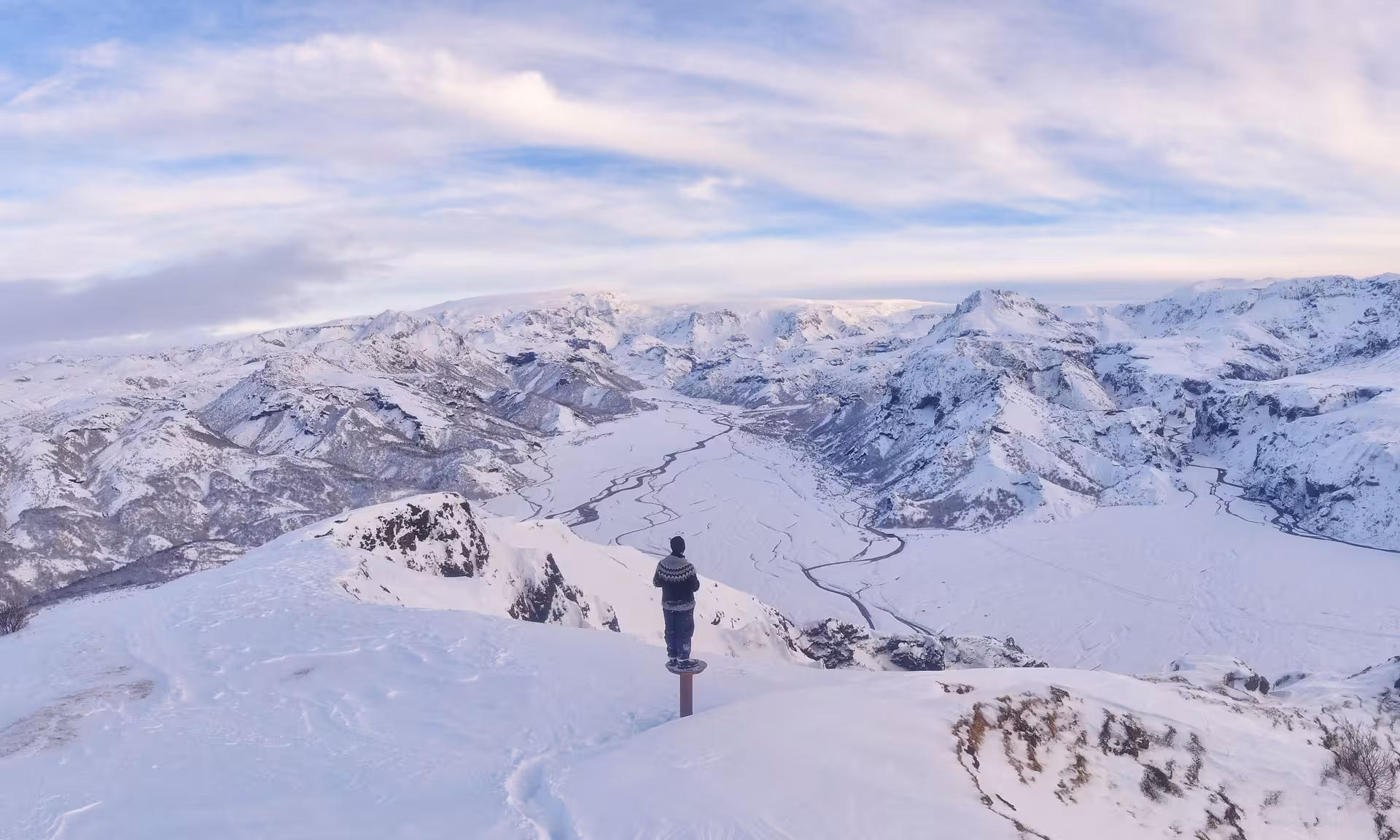 Hiker standing on snowy summit overlooking Thorsmork valley and glacial mountains in Iceland