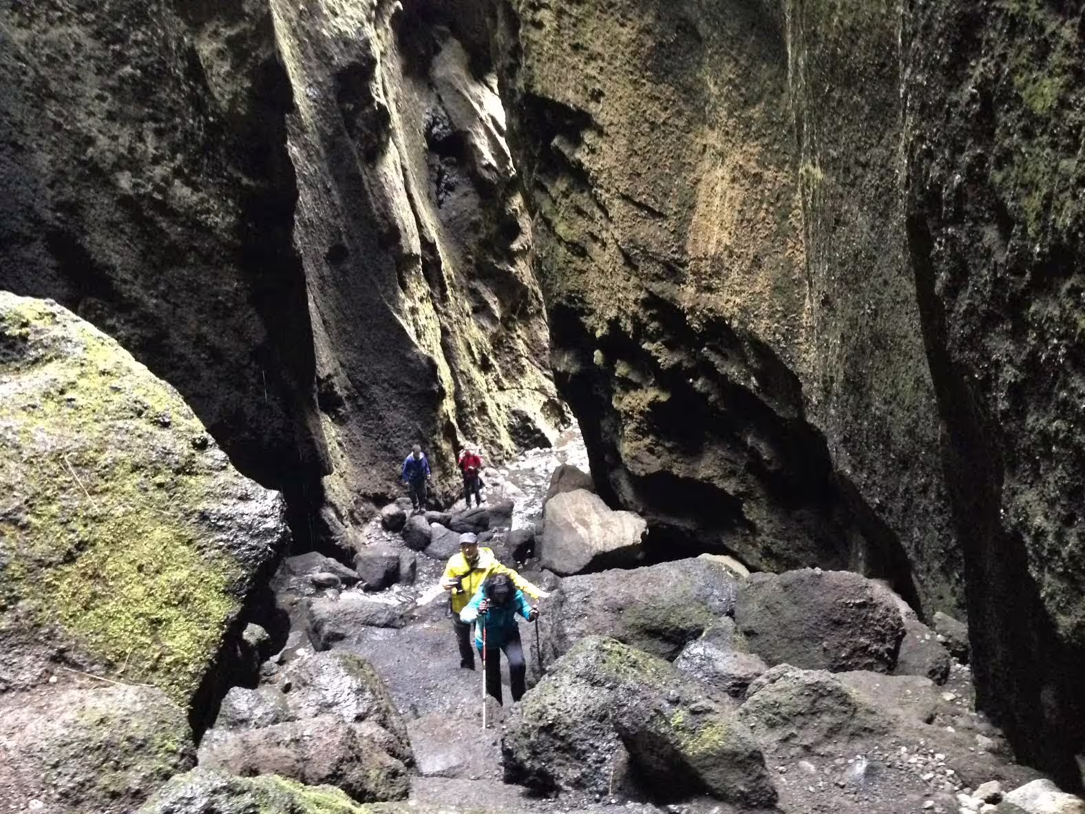 Hikers navigating rocky canyon trail in Thorsmork, Iceland, with moss-covered volcanic walls