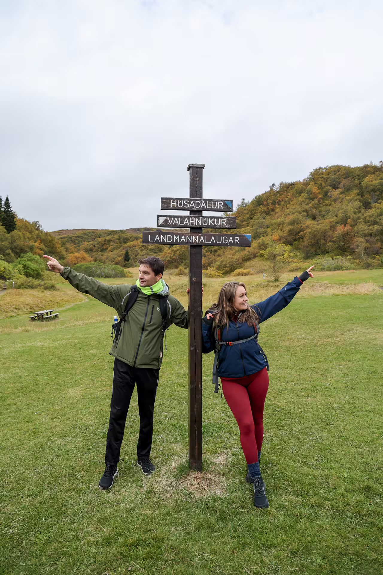 Excited hikers posing at Thorsmork trailhead signpost pointing to Landmannalaugar on a scenic full-day 4x4 Iceland adventure tour