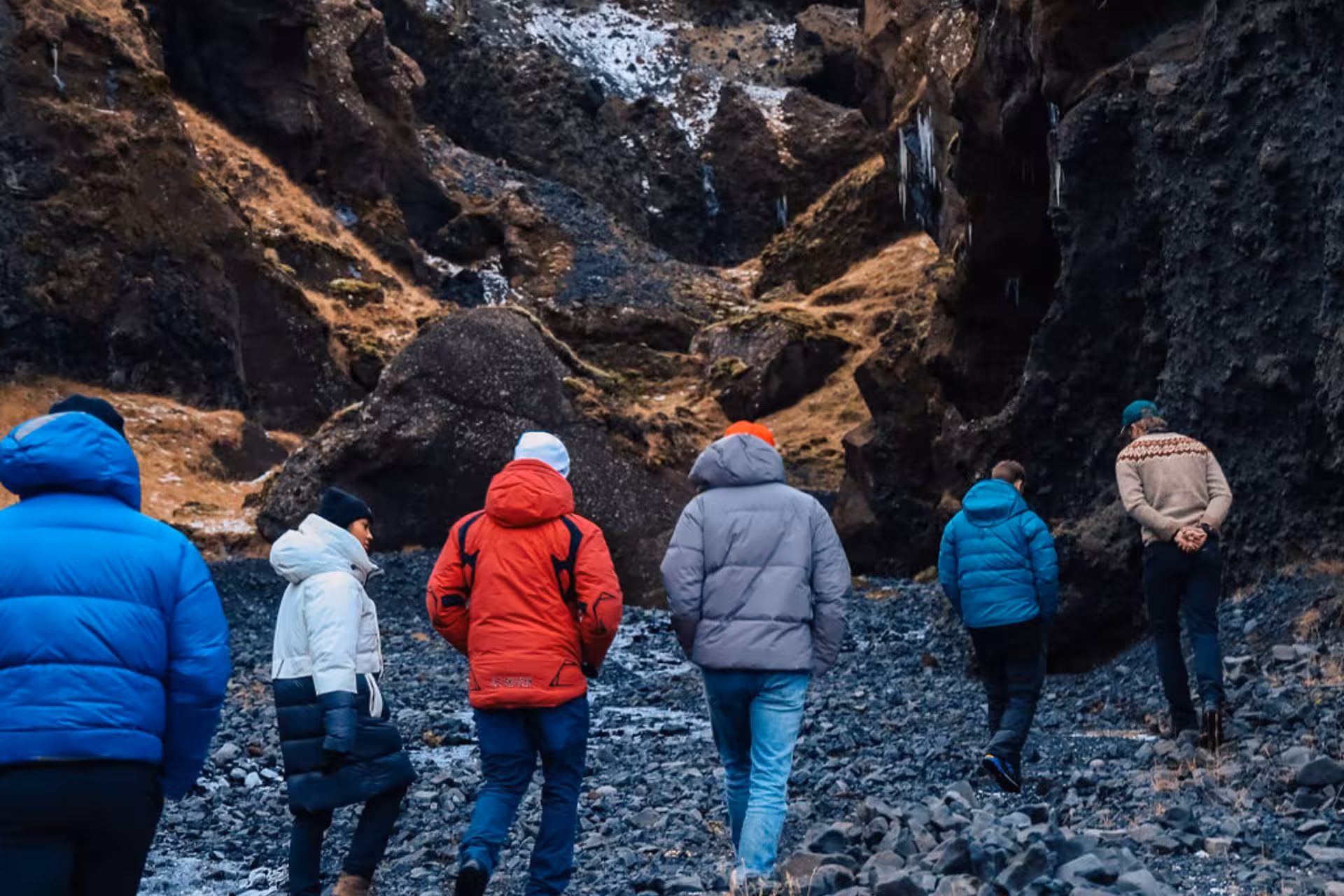 Group of tourists hiking through a narrow volcanic canyon with frozen waterfalls in Thorsmork highlands
