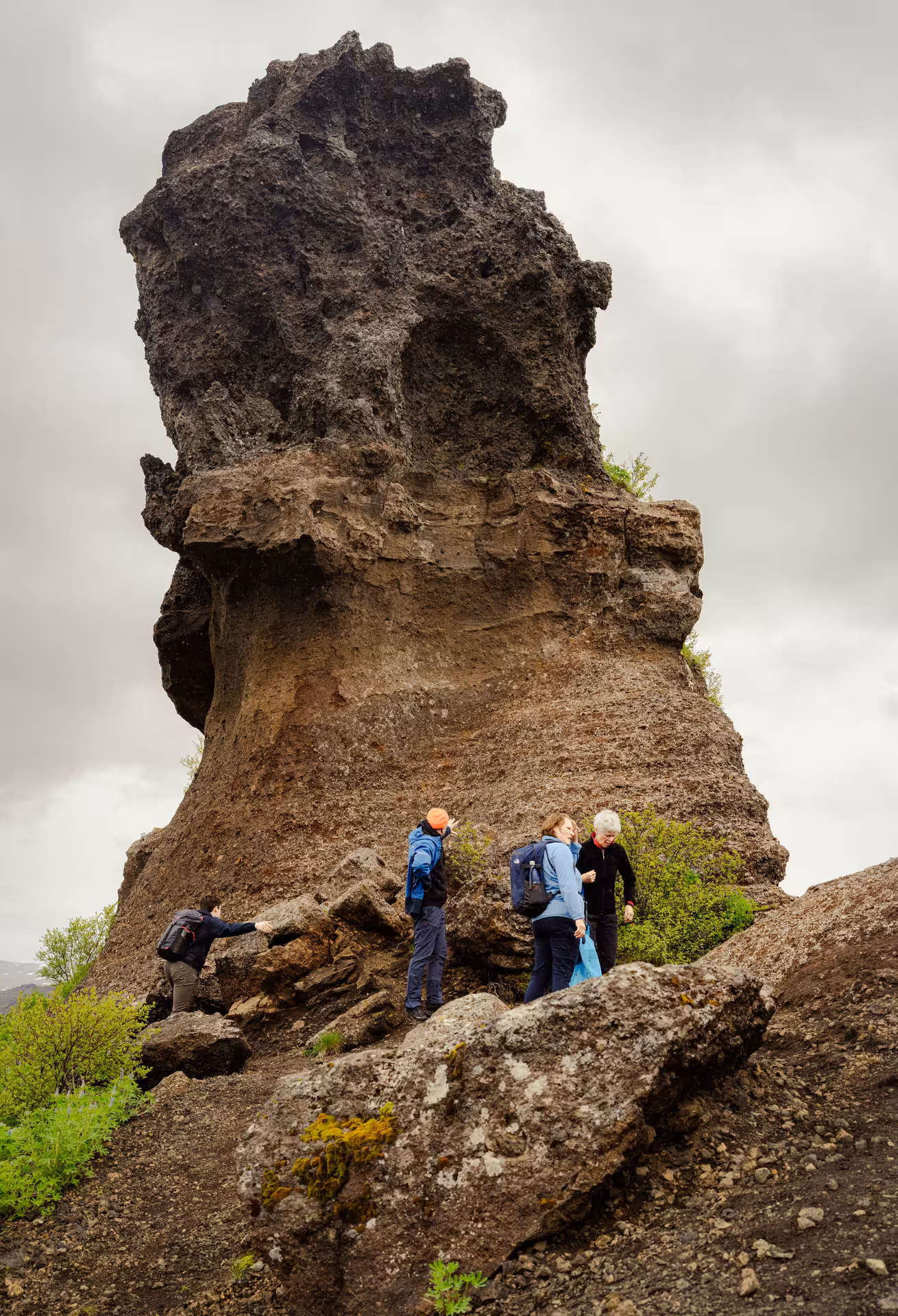 Hikers exploring a towering volcanic rock formation in Thorsmork on a cloudy day