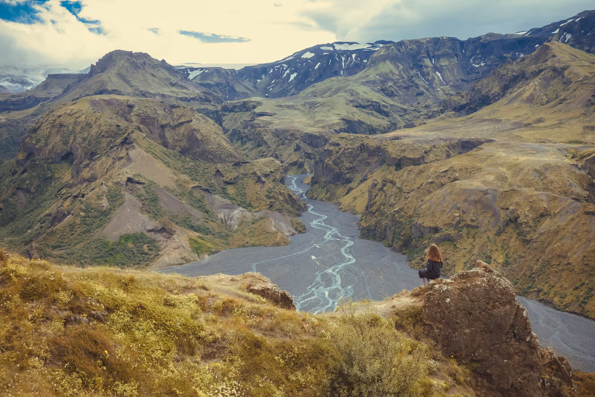 Hiker sitting on rock overlooking Thorsmork canyon river valley with snow-capped mountains in Iceland