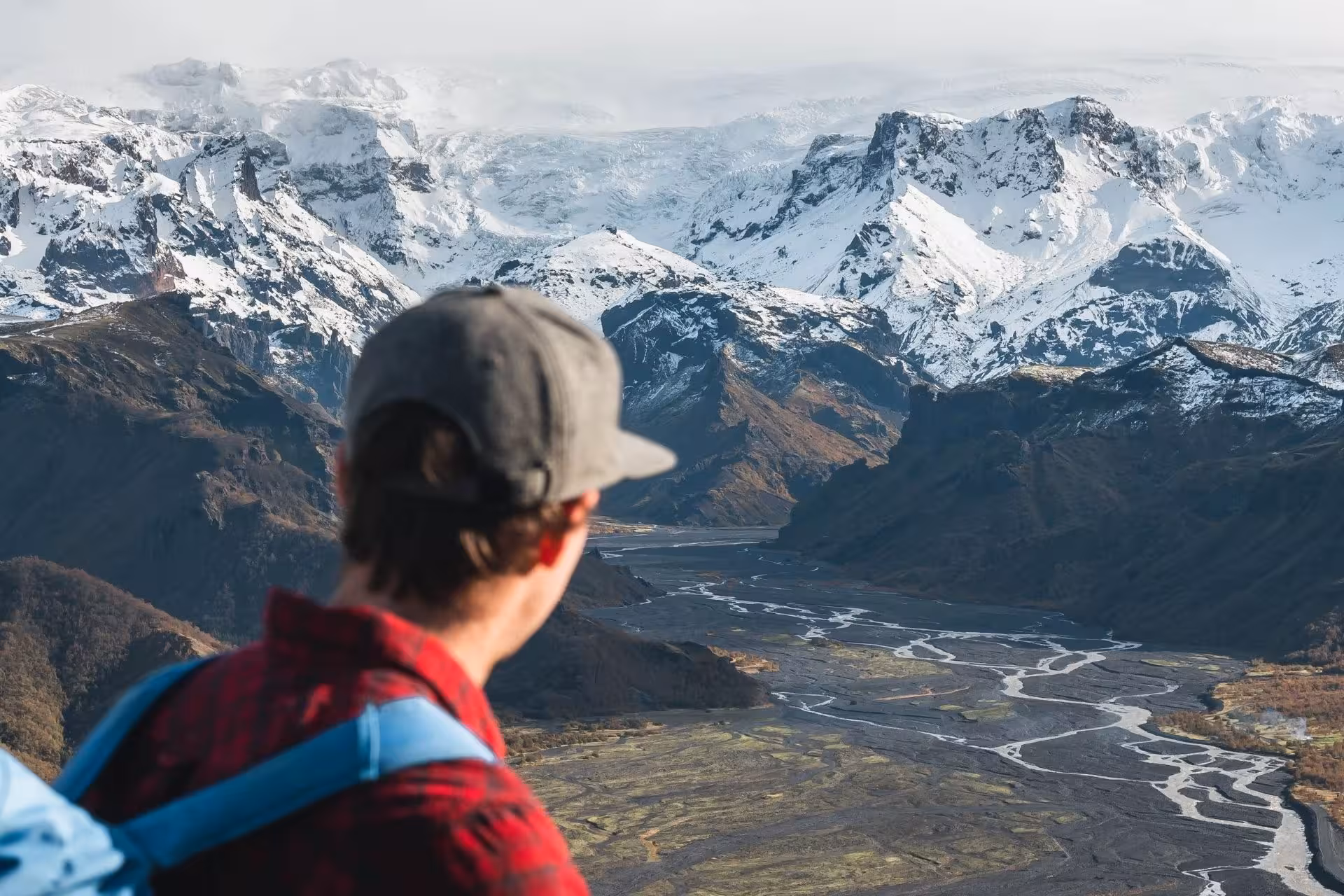 Hiker overlooking Thorsmork valley with braided glacial rivers and snow-capped mountains in Iceland