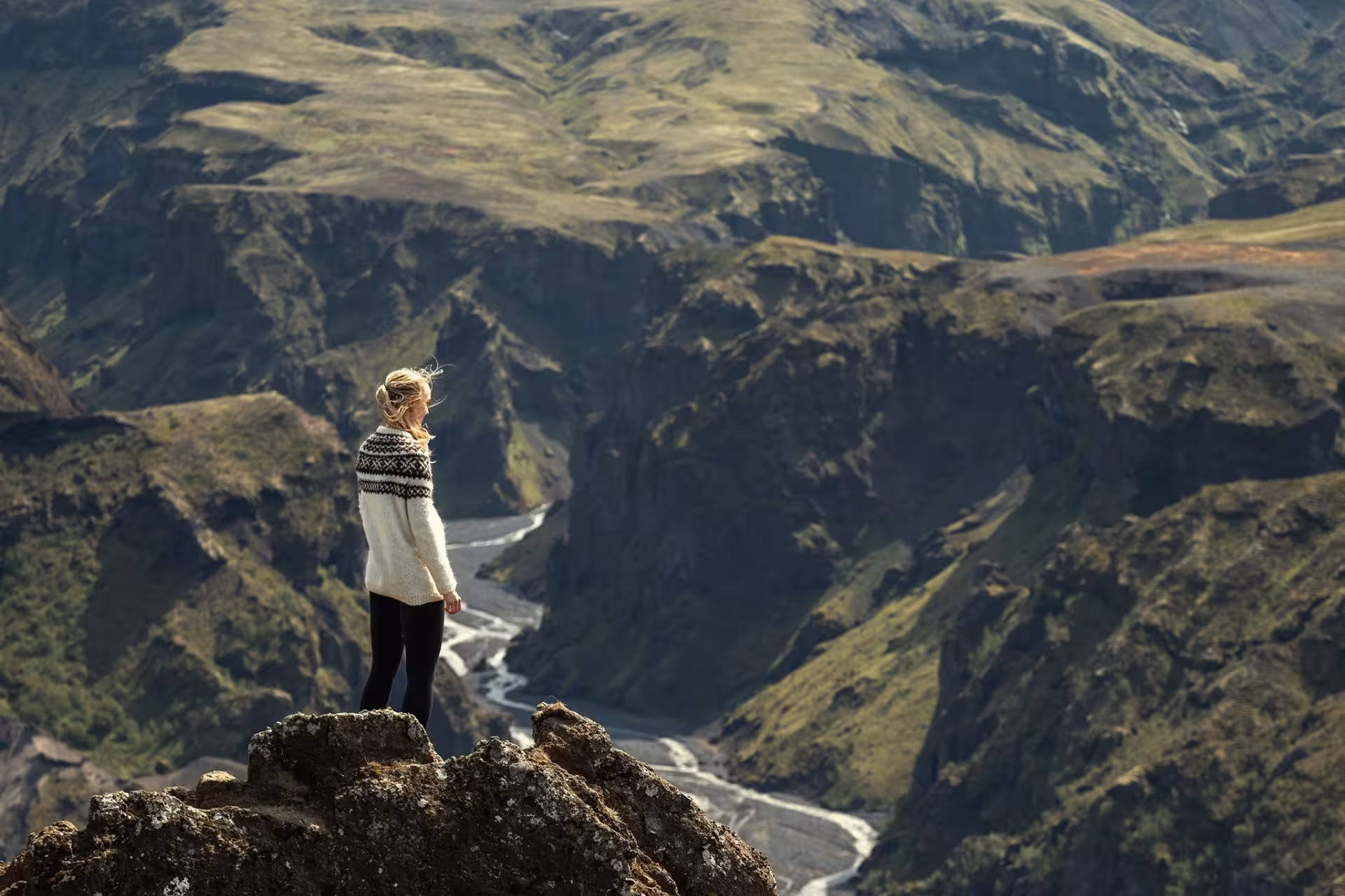 Hiker standing on rocky summit overlooking Thorsmork valley and winding glacial river, Iceland