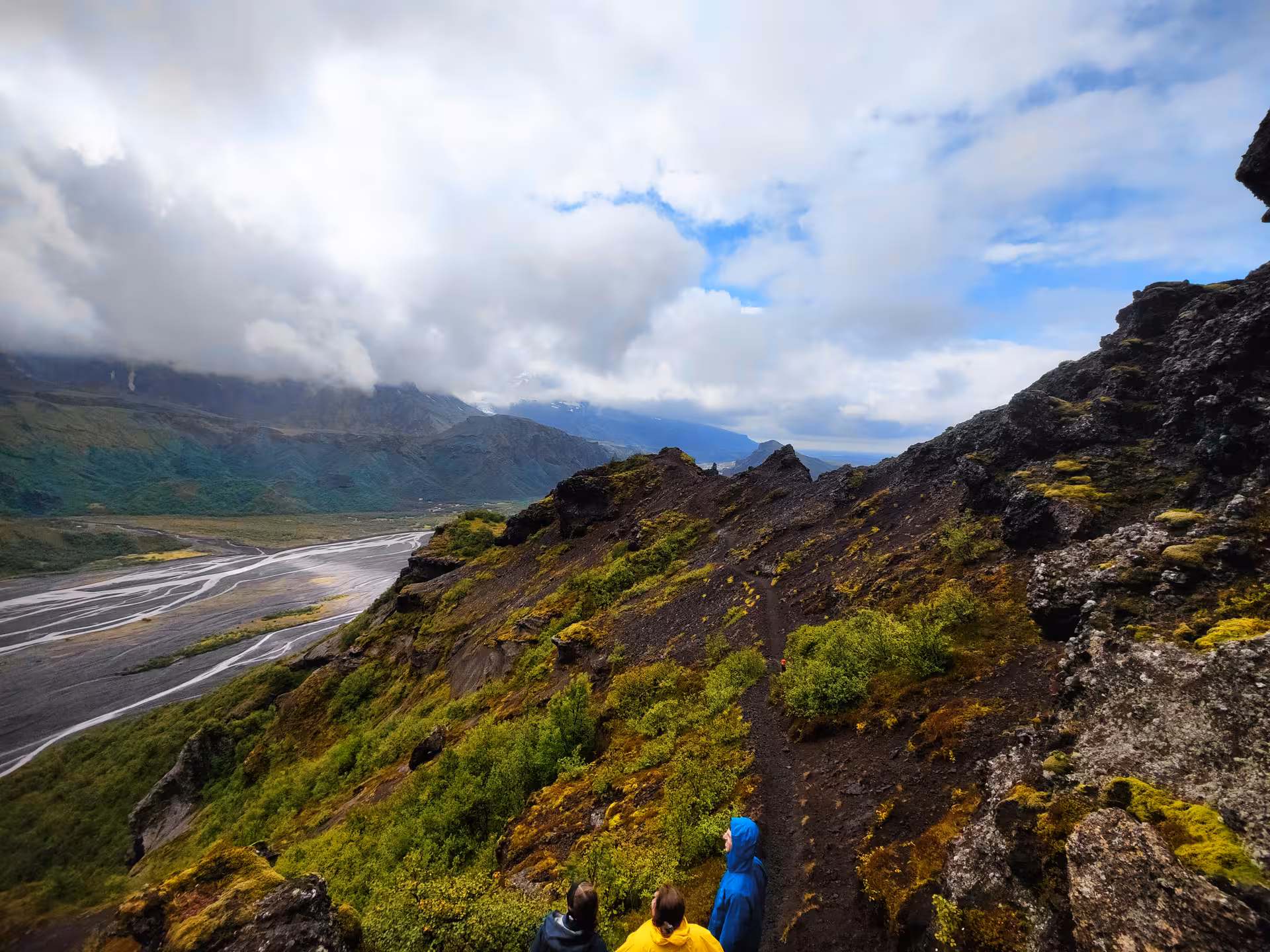 Hikers on a mossy volcanic ridge overlooking a braided glacial river valley in Thorsmork, Iceland